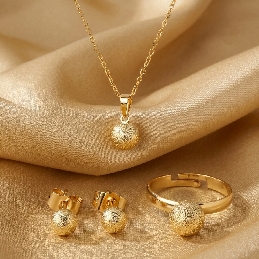 Gold jewelry set including necklace, earrings, and ring on beige fabric with 'JOLI' branding.